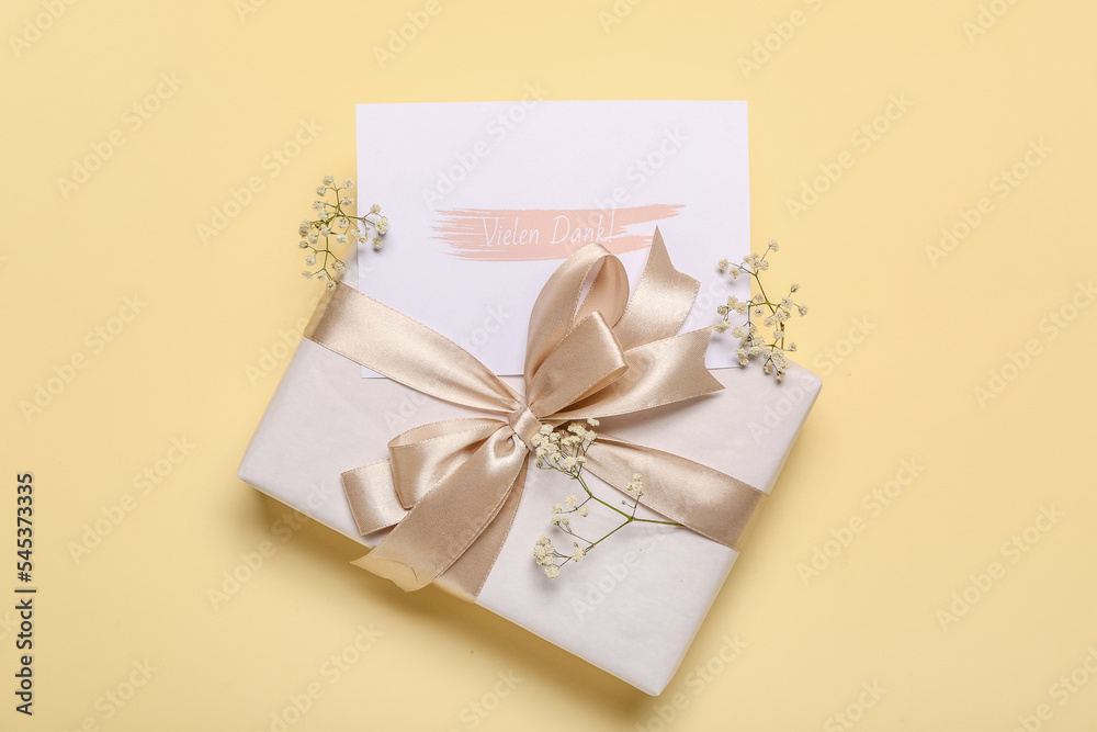 Card with text VIELEN DANK, flowers and gift box on beige background Card with text VIELEN DANK, flowers and gift box on beige background