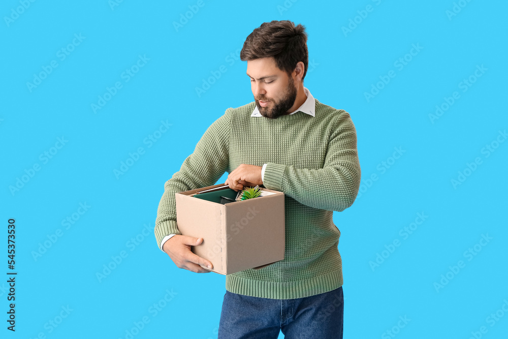 Fired young man holding box with personal stuff on blue background Fired young man holding box with personal stuff on blue background
