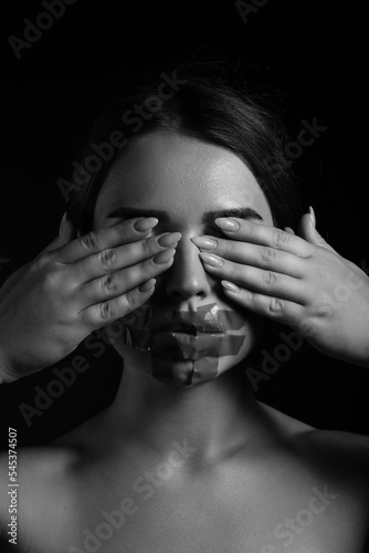Fototapeta Naklejka Na Ścianę i Meble -  Young woman with taped mouth covering her eyes on dark background. Censorship concept