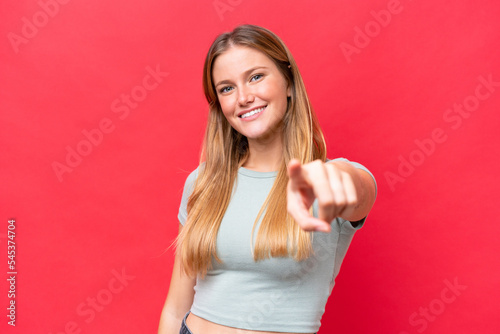 Young beautiful woman isolated on red background pointing front with happy expression © luismolinero