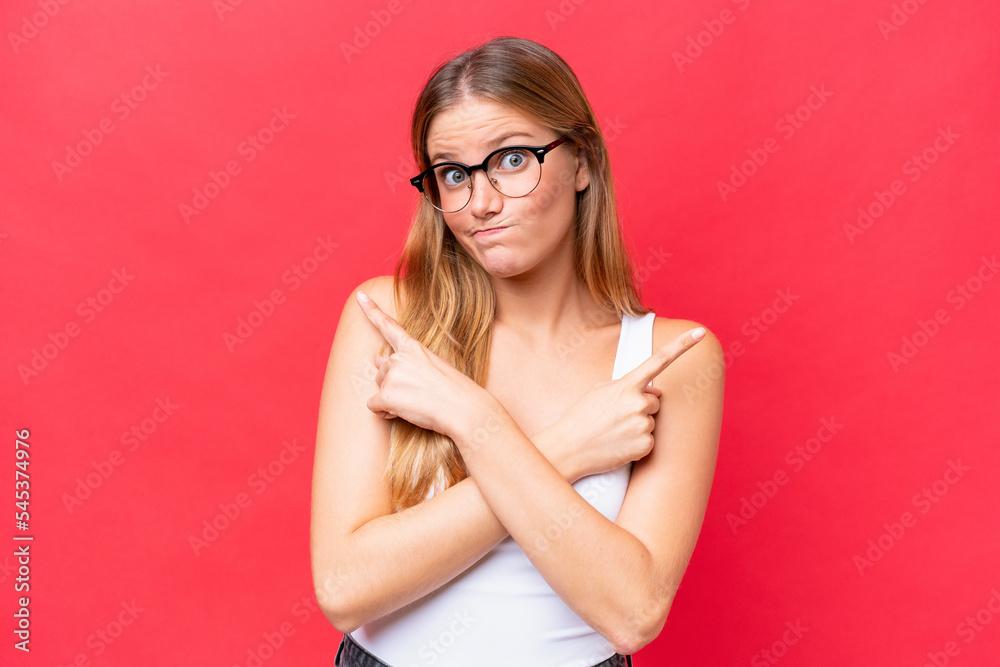 Young beautiful woman isolated on red background pointing to the laterals having doubts Young beautiful woman isolated on red background pointing to the laterals having doubts