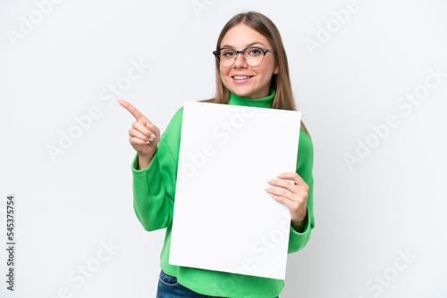 Young caucasian woman isolated on white background holding an empty placard and pointing side