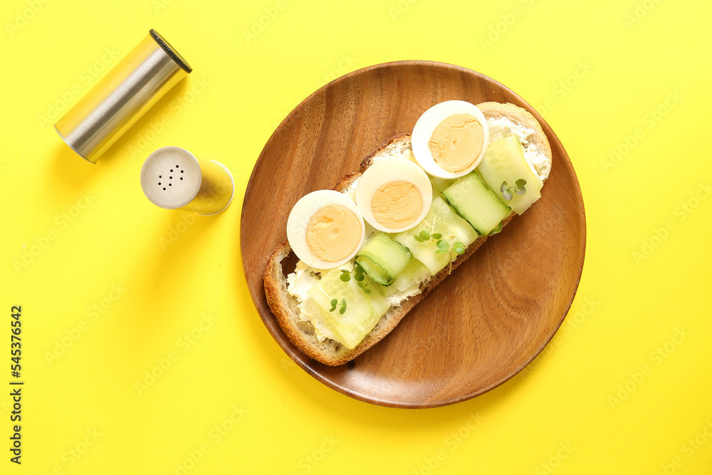 Wooden plate of tasty toast with boiled egg and cucumber on yellow background Wooden plate of tasty toast with boiled egg and cucumber on yellow background