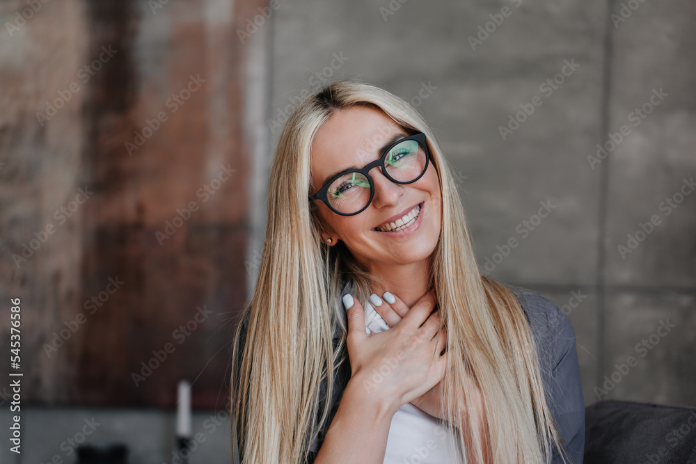 Close up portrait of adorable blonde Swedish young woman in spectacles toothy smiling looks at camera folded hands on chest with grateful facial expression. Pretty Caucasian girl in appreciation. Close up portrait of adorable blonde Swedish young woman in spectacles toothy smiling looks at camera folded hands on chest with grateful facial expression. Pretty Caucasian girl in appreciation.