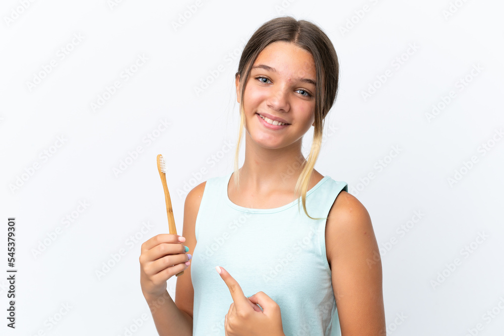 Little caucasian girl holding a toothbrush isolated on white background and pointing it