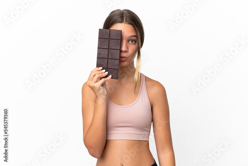 Little caucasian girl isolated on white background taking a chocolate tablet and surprised