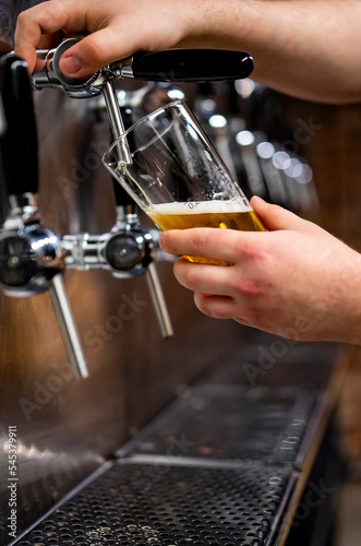 bartender hand at beer tap pouring a draught beer in glass serving in a bar or pub. taproom