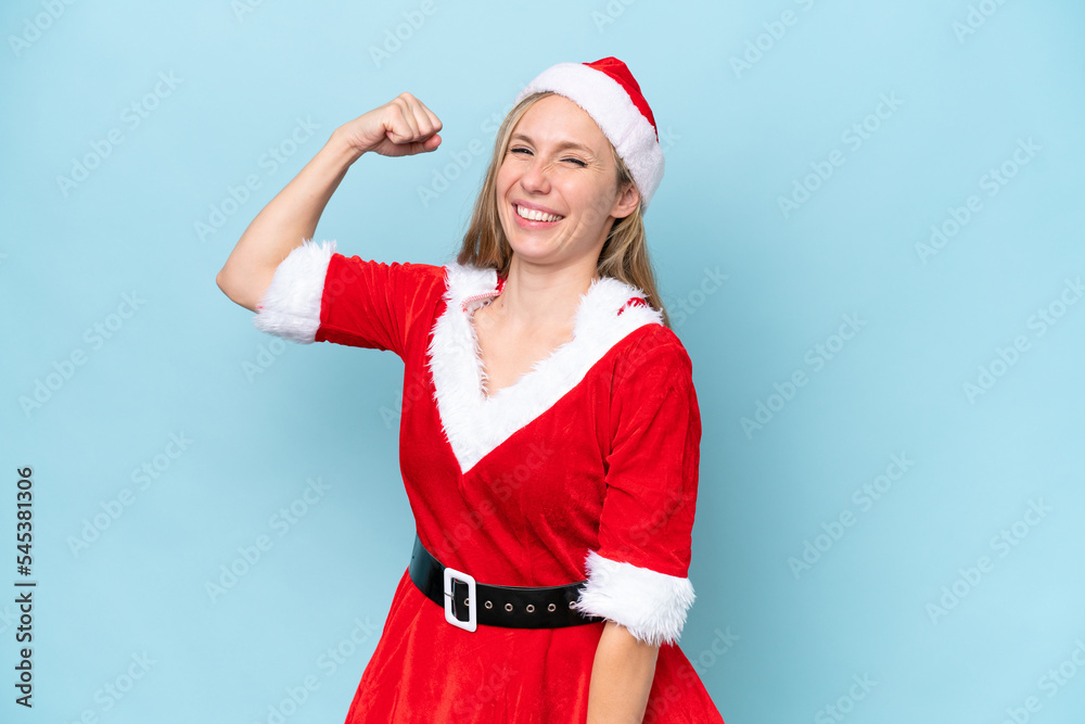 Young blonde woman dressed as mama claus isolated on blue background doing strong gesture