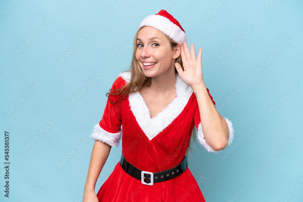Young blonde woman dressed as mama claus isolated on blue background listening to something by putting hand on the ear Young blonde woman dressed as mama claus isolated on blue background listening to something by putting hand on the ear