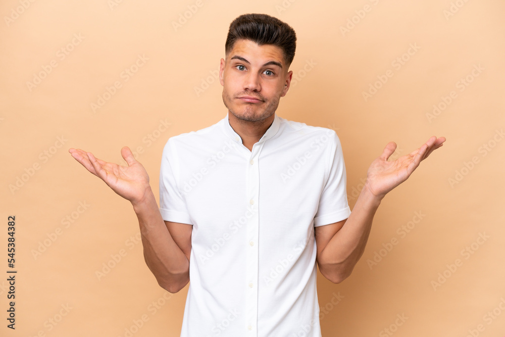 Young caucasian man isolated on beige background making doubts gesture Young caucasian man isolated on beige background making doubts gesture