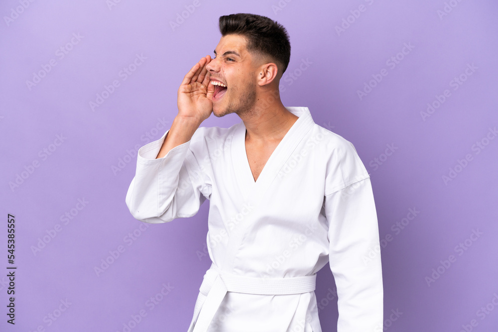 Young caucasian man doing karate isolated on purple background shouting with mouth wide open to the side Young caucasian man doing karate isolated on purple background shouting with mouth wide open to the side