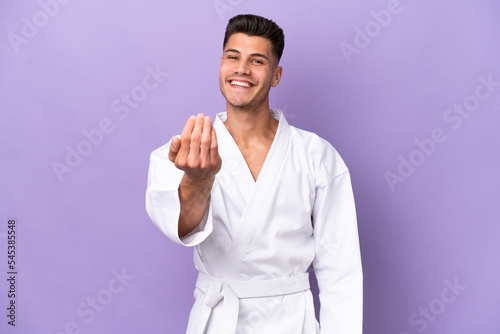 Young caucasian man doing karate isolated on purple background inviting to come with hand. Happy that you came