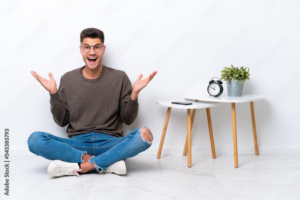 Young caucasian man sitting in his home isolated on white background with shocked facial expression Young caucasian man sitting in his home isolated on white background with shocked facial expression