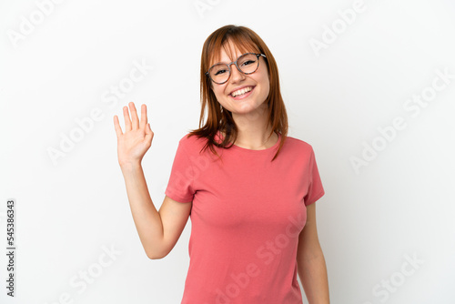 Redhead girl isolated on white background saluting with hand with happy expression
