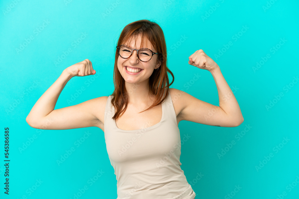 Redhead girl isolated on blue background doing strong gesture Redhead girl isolated on blue background doing strong gesture