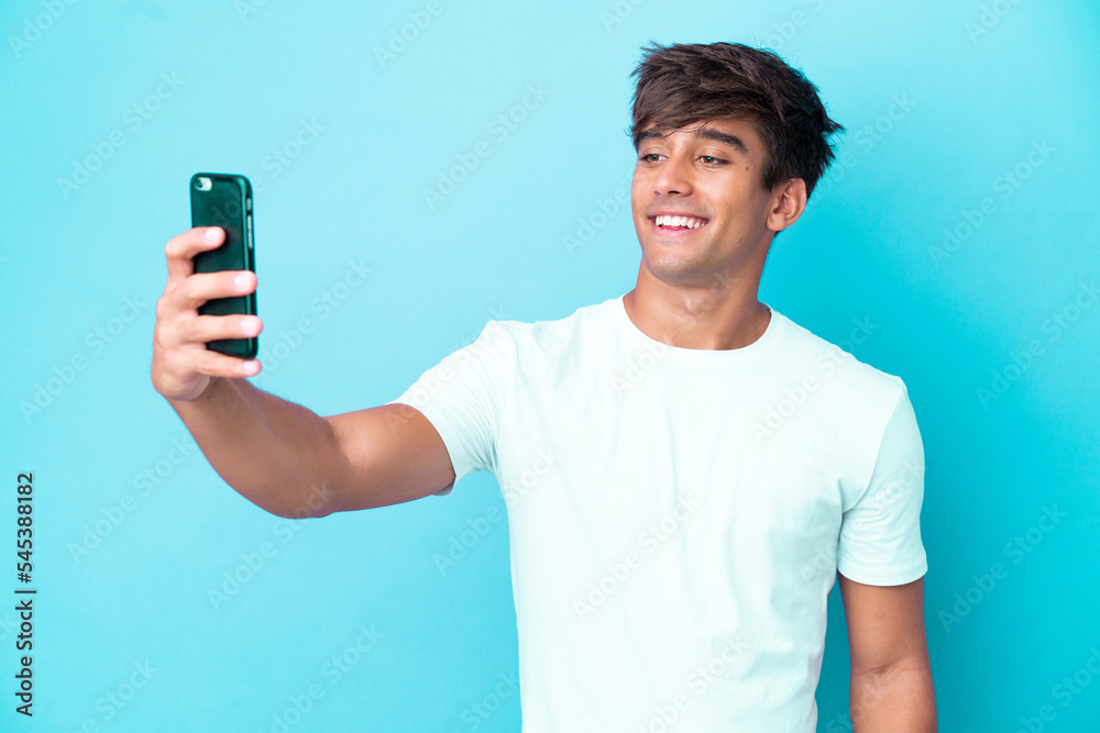 Young caucasian man isolated on blue background making a selfie with mobile phone Young caucasian man isolated on blue background making a selfie with mobile phone