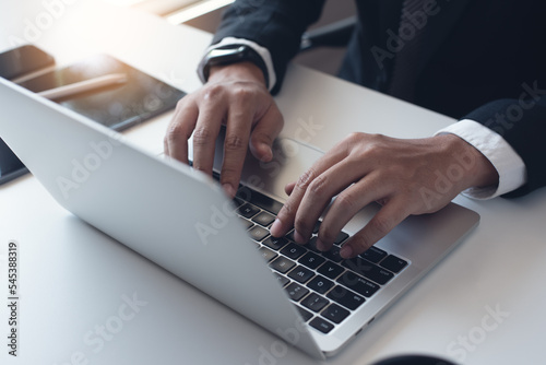 Close up of businessman working with laptop computer on table at office. Business man hands typing on laptop, online working, surfing the internet