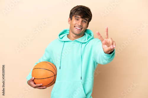 Handsome young basketball player man isolated on ocher background smiling and showing victory sign © luismolinero