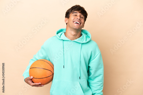 Handsome young basketball player man isolated on ocher background laughing