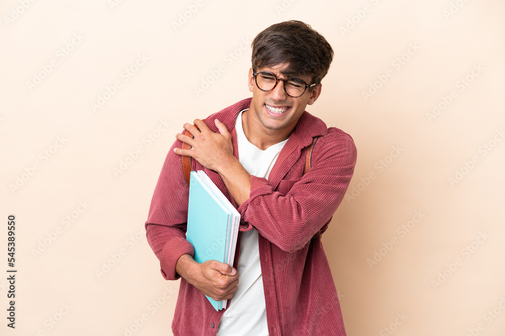 Young student caucasian man isolated on ocher background suffering from pain in shoulder for having made an effort Young student caucasian man isolated on ocher background suffering from pain in shoulder for having made an effort