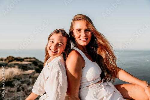 Sea family vacation together, happy mom and teenage daughter hugging and smiling together over sunset sea view. Beautiful woman with long hair relaxing with her child. Concept of happy friendly family photo