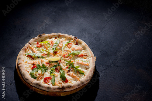 Pizza with salmon, mozzarella, cherry tomatoes, arugula, lemon and parmesan. Italian cuisine. On a black background. Free space for text. View from above.