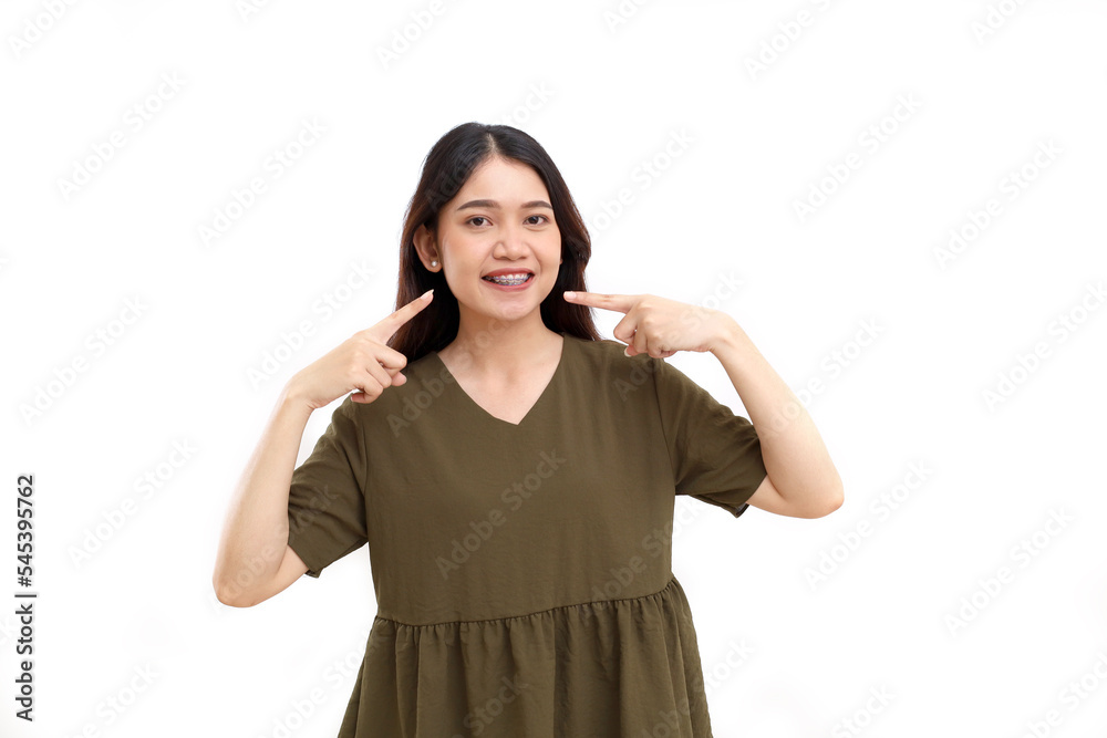 Happy beautiful young asian woman standing while pointing her mouth and braces teeth. Isolated on white Happy beautiful young asian woman standing while pointing her mouth and braces teeth. Isolated on white