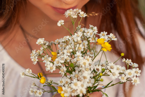 Bouquet of wild flowers against background of long-haired girl smelling them