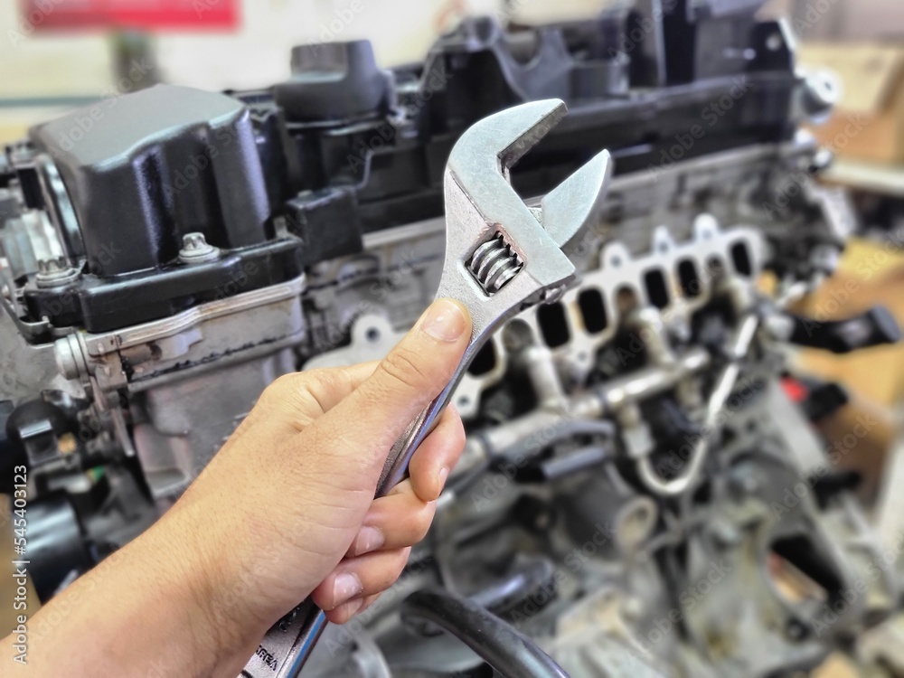 Naklejka premium Mechanic holding wrench for car engine repair with blur background
