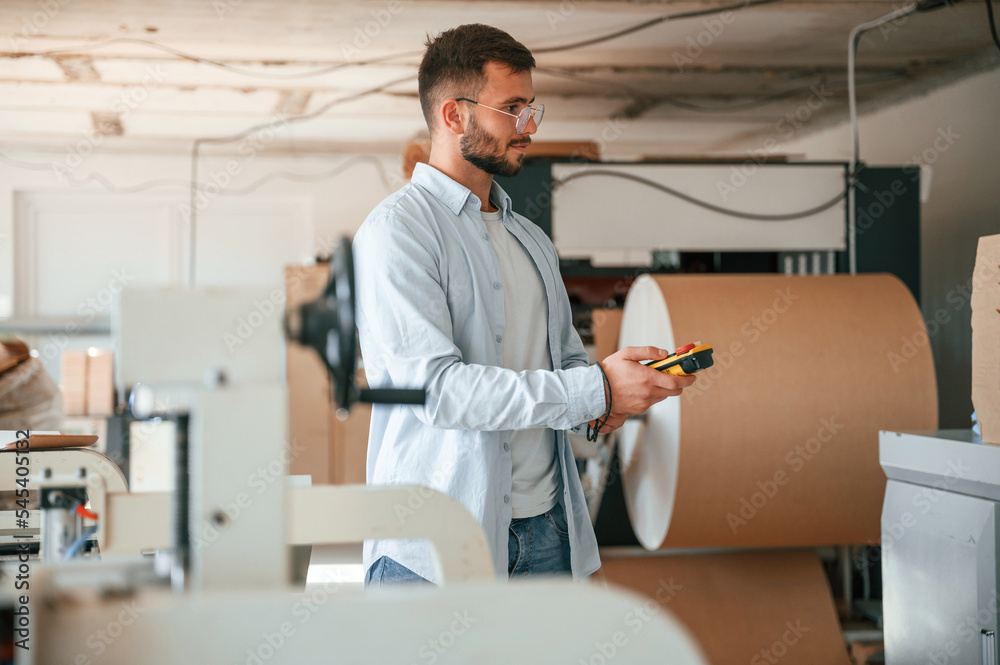 Holding controller of printing machine. Polygraph worker in white clothes is indoors Holding controller of printing machine. Polygraph worker in white clothes is indoors