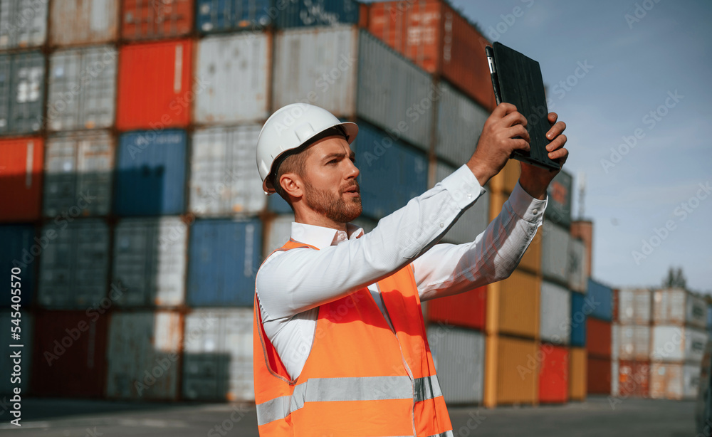 Taking photos by using tablet. Male worker is on the location with containers Taking photos by using tablet. Male worker is on the location with containers