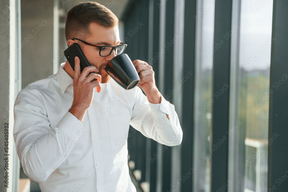 Holding cup of drink. Man in formal clothes is working in the modern office Holding cup of drink. Man in formal clothes is working in the modern office