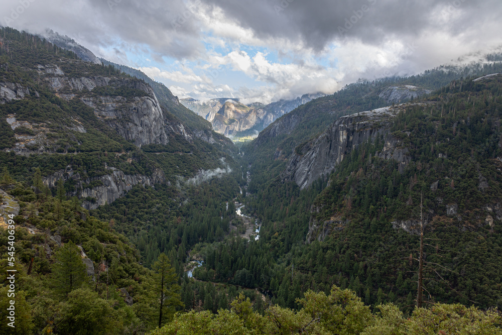 Fototapeta premium Valley in Yosemeti National Park with conifers, low clouds, cloudy sky and patches of fog, California, USA