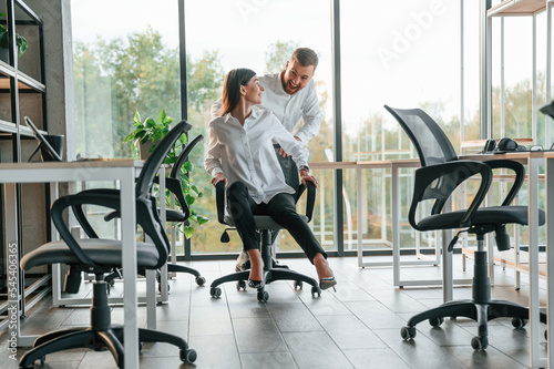 Having fun by riding the chair. Man and woman are working in the modern office together