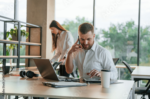 Boss is having conversation by the phone. Man and woman are working in the modern office together