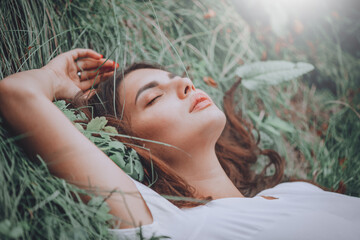 Young woman lying on the grass. Beauty woman lying on the field and looking on camera. Beautiful brunette Girl lying on the meadow, relaxing. Enjoying nature. Spring or Summer Green Grass. Freedom