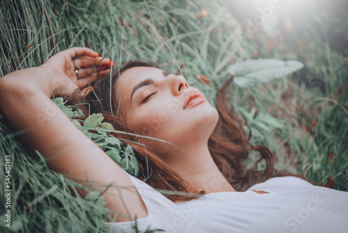 Young woman lying on the grass. Beauty woman lying on the field and looking on camera. Beautiful brunette Girl lying on the meadow, relaxing. Enjoying nature. Spring or Summer Green Grass. Freedom