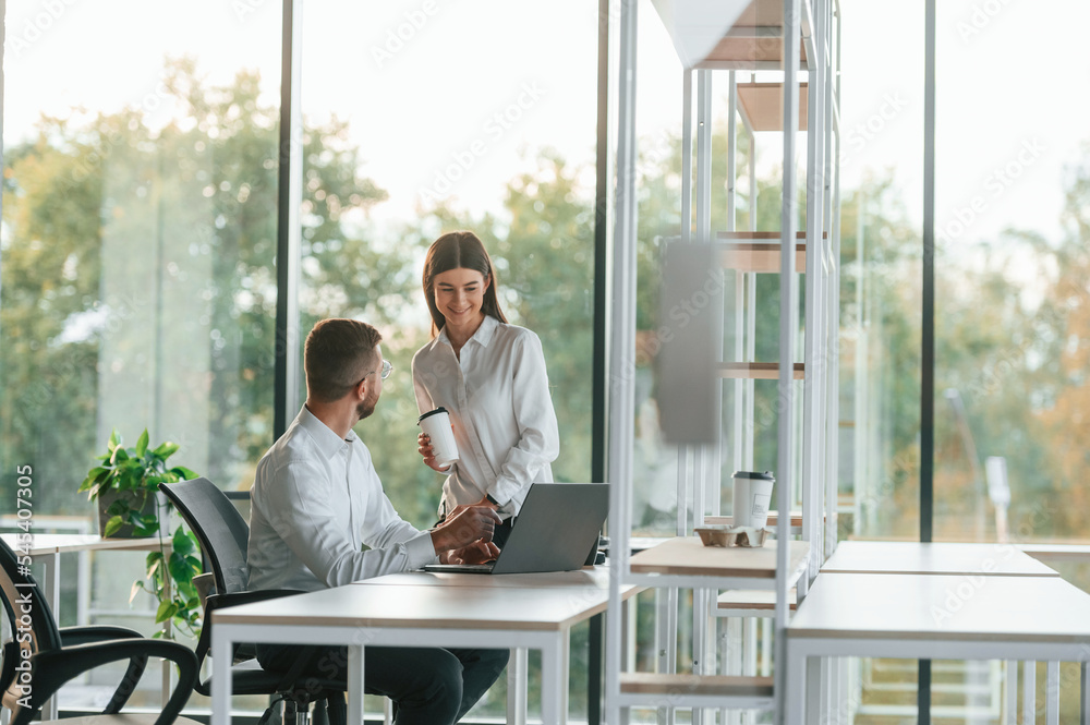 Working by using laptop. Man and woman are in the modern office together Working by using laptop. Man and woman are in the modern office together