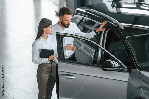 Opening the door. Man with woman in white clothes are in the car dealership together © standret