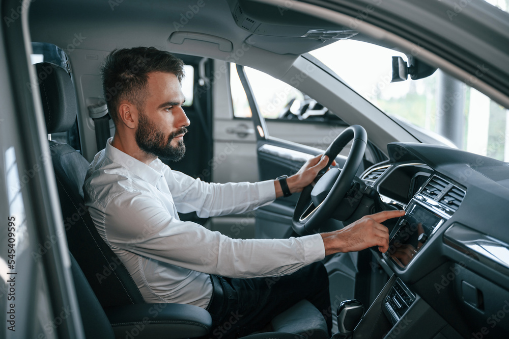 Examining the salon of the automobile. Young man in white clothes is in the car dealership Examining the salon of the automobile. Young man in white clothes is in the car dealership