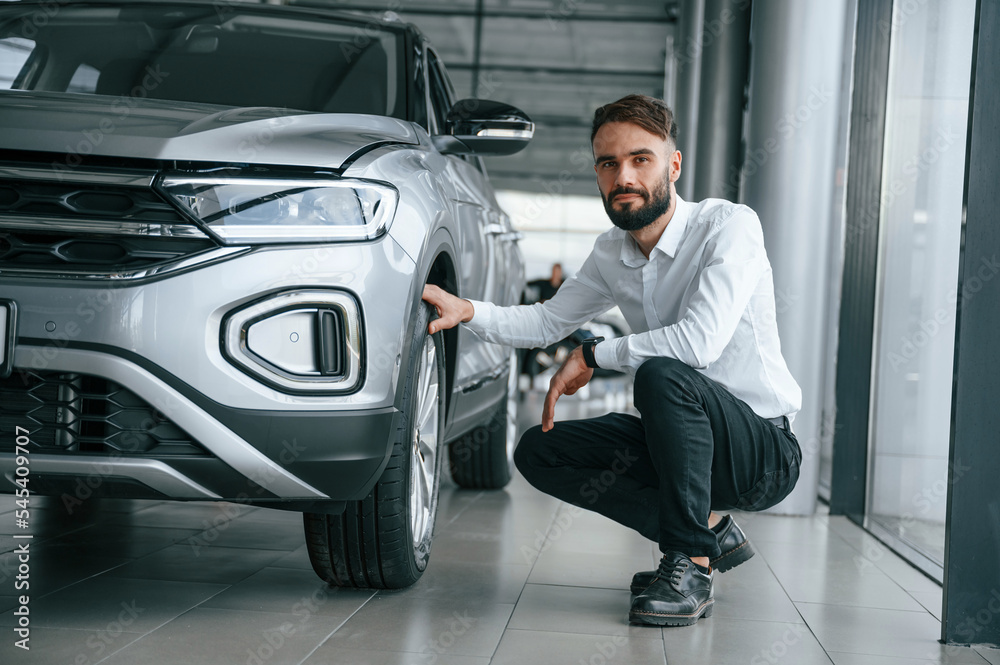 Checking the tires. Young man in white clothes is in the car dealership Checking the tires. Young man in white clothes is in the car dealership