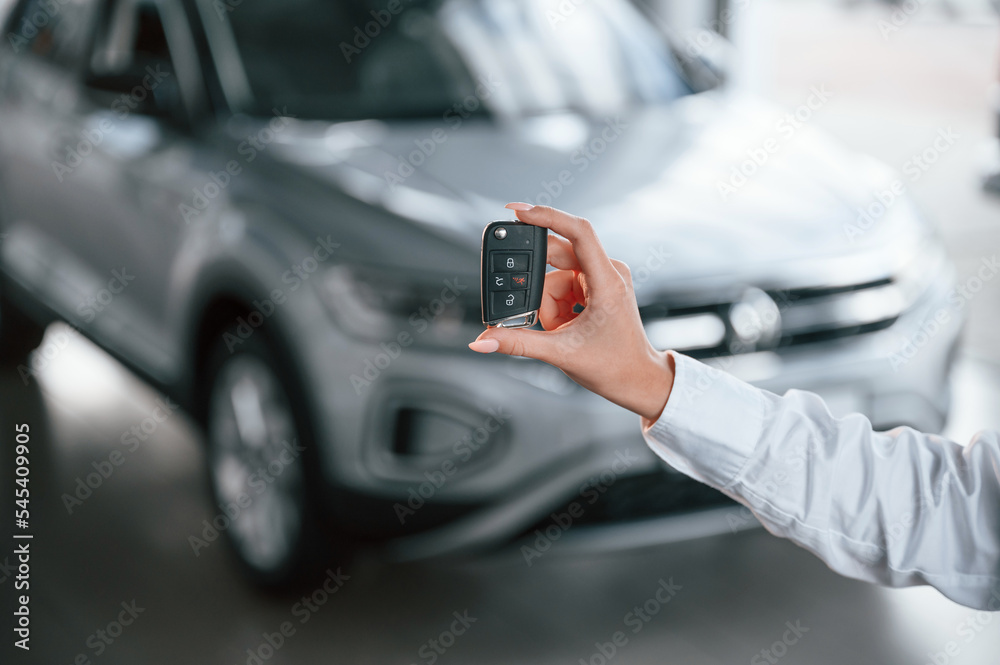 Close up view of keys. Young woman in white formal clothes is in the at dealership Close up view of keys. Young woman in white formal clothes is in the at dealership