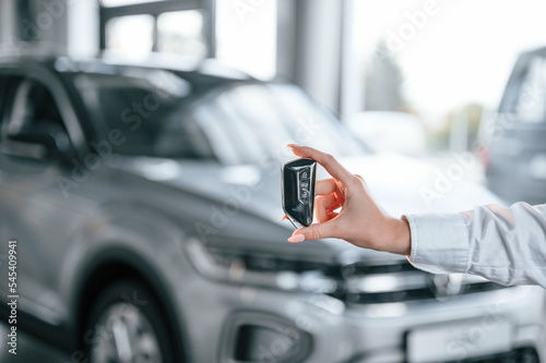 Close up view of keys. Young woman in white formal clothes is in the at dealership