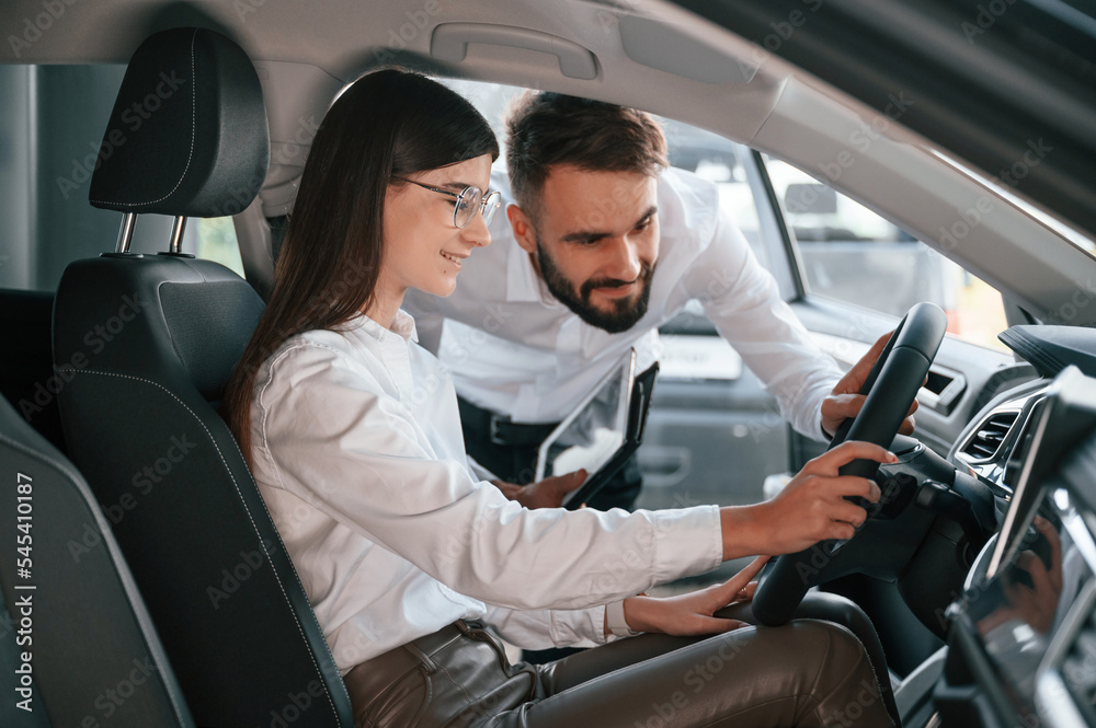 Woman sitting in the automobile. Man in white clothes are in the car dealership Woman sitting in the automobile. Man in white clothes are in the car dealership