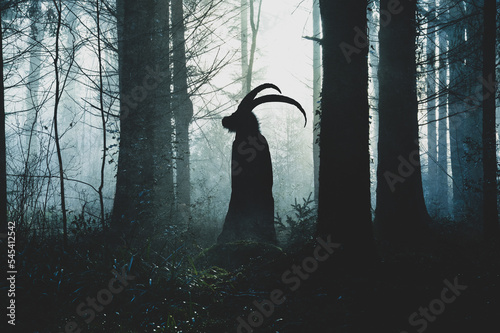 A fantasy concept of a pagan horned goat like figure. Silhouetted against the light. In a spooky forest in winter. With a textured edit.