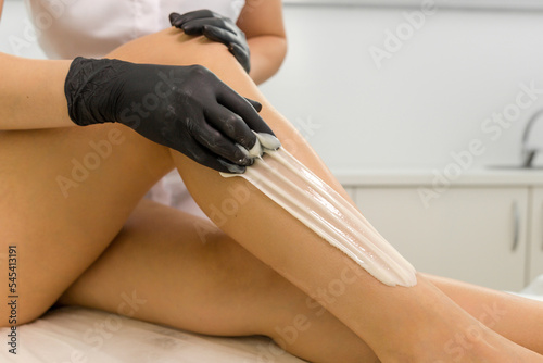 Epilation of hair on the legs in a beauty salon close-up.  Beautician applying wax on legs photo