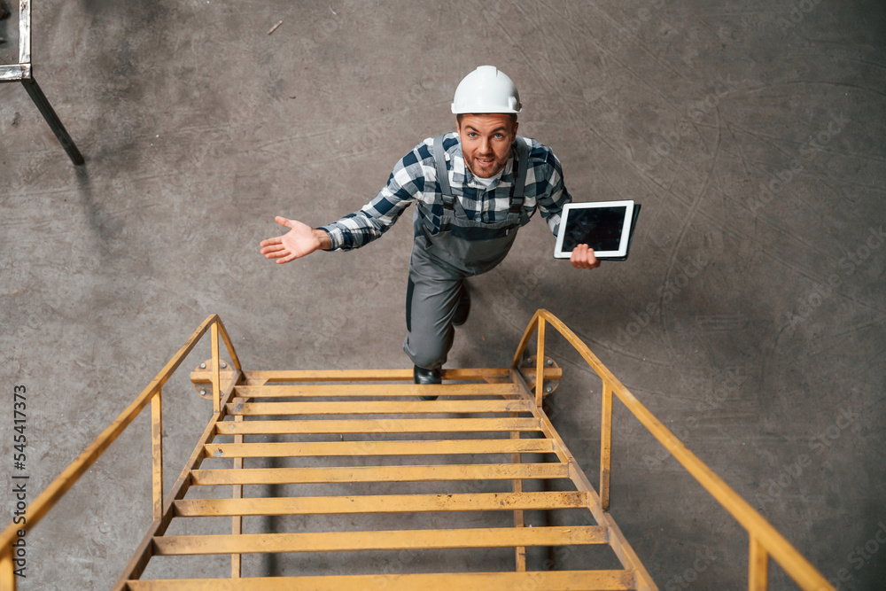 View from the top of ladder. Factory male worker in uniform is indoors View from the top of ladder. Factory male worker in uniform is indoors
