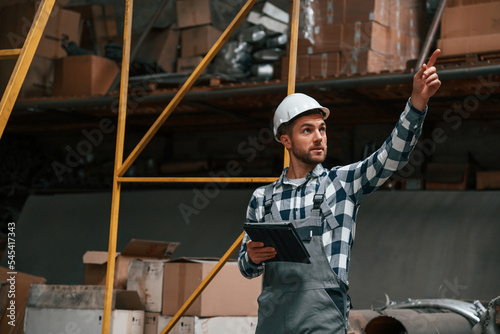 Showing something to the other employees. Factory male worker in uniform is indoors