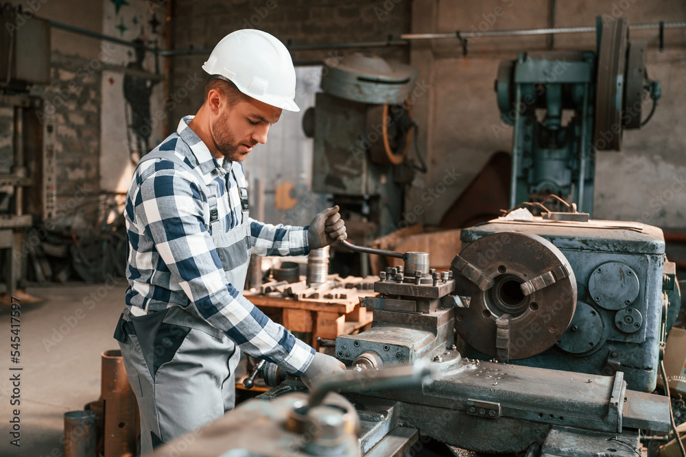 Side view. Operating the machine. Factory male worker in uniform is indoors Side view. Operating the machine. Factory male worker in uniform is indoors