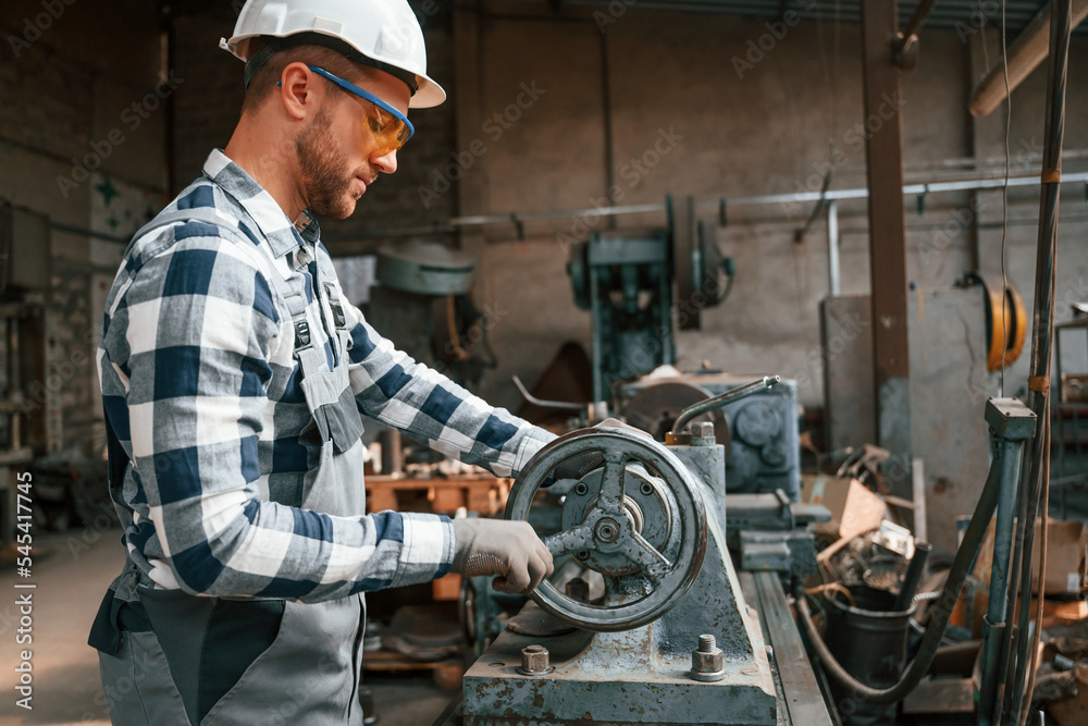 Focused on work with factory machine. Worker in uniform is indoors Focused on work with factory machine. Worker in uniform is indoors